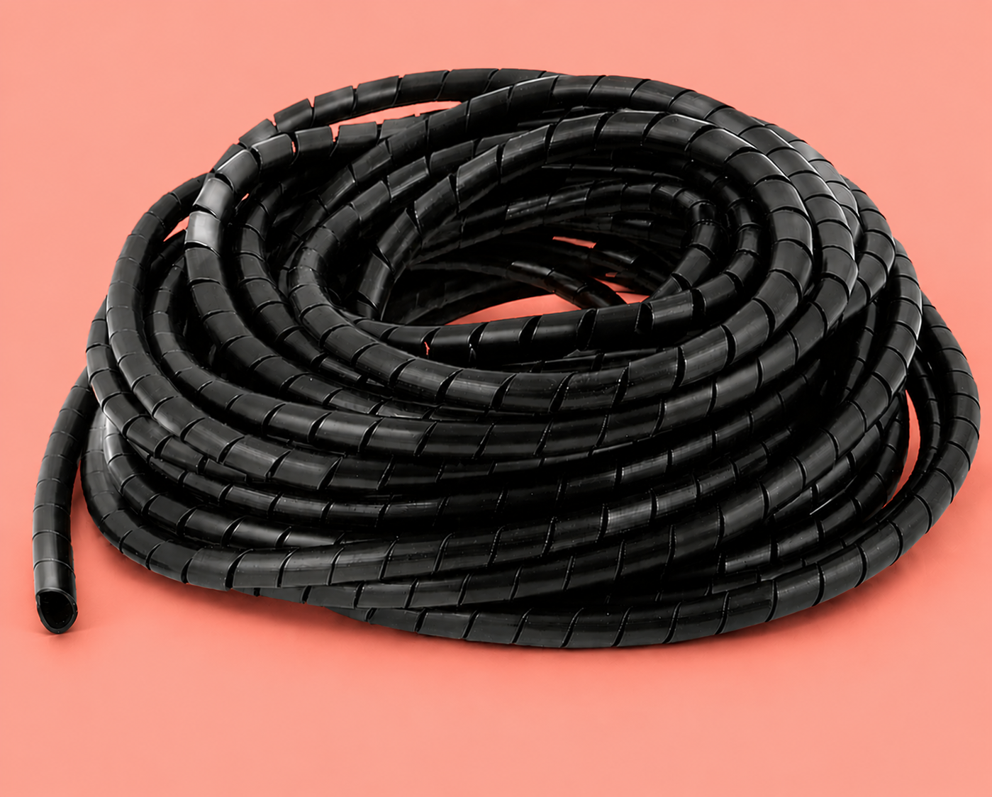 Black spiral cable organizer coiled on a salmon color background, flexible wire management sleeve with segmented design for organizing computer and electronic cables