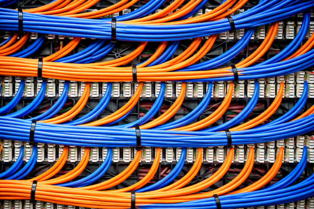 Blue and orange network cables neatly bundled with black zip ties inside a telecommunications or server patch panel.